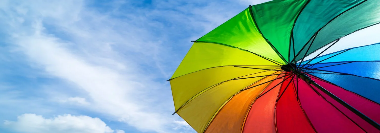 Colorful rainbow umbrella on blue sky background. LGBT, Pride Month, diversity, Sunprotect Concept.
